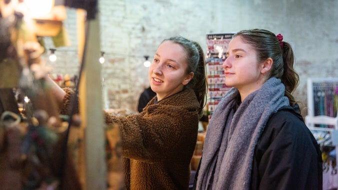 Two women explore the indoor Christmas market at Calke Abbey. They're seen here looking and touching products displayed on one of the stalls.